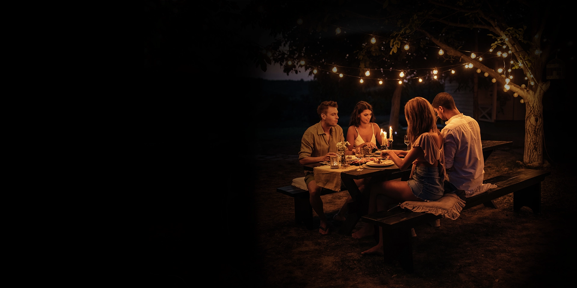 Zwei Pärchen genießen ein romantisches Candle-Light-Dinner im Freien, direkt neben ihrem Wohnmobil, umgeben von einer gemütlichen Atmosphäre und der ruhigen Natur.